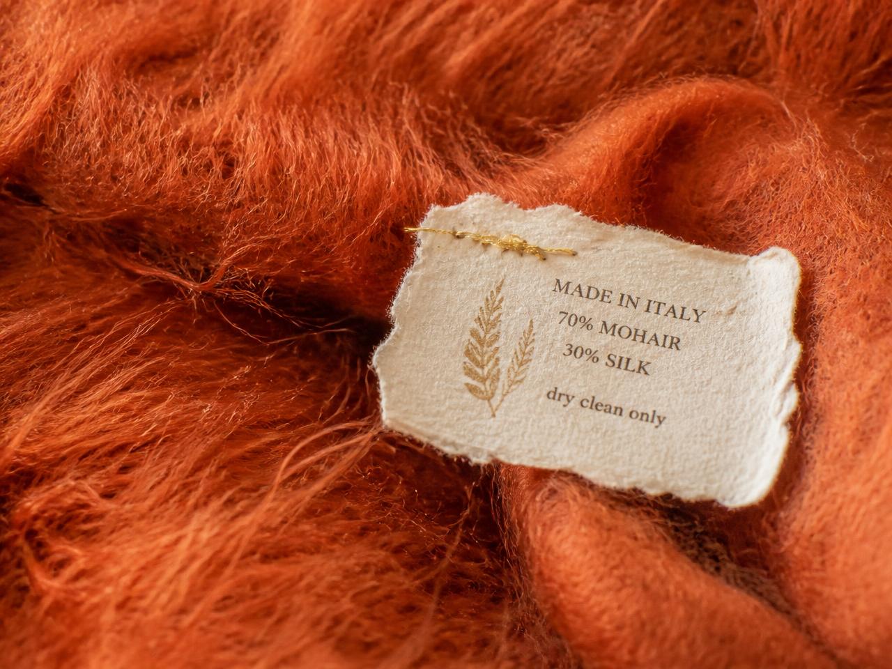 Macro of terracotta mohair with a deckled paper tag and gold thread